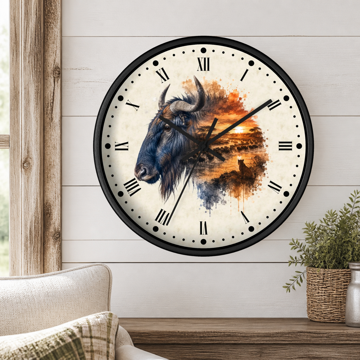 A large round wall clock with a black frame and Roman numerals, mounted on a white shiplap wall above a wooden table. The clock face features a painted Wildebeest head on the left and a warm orange sunset landscape on the right.