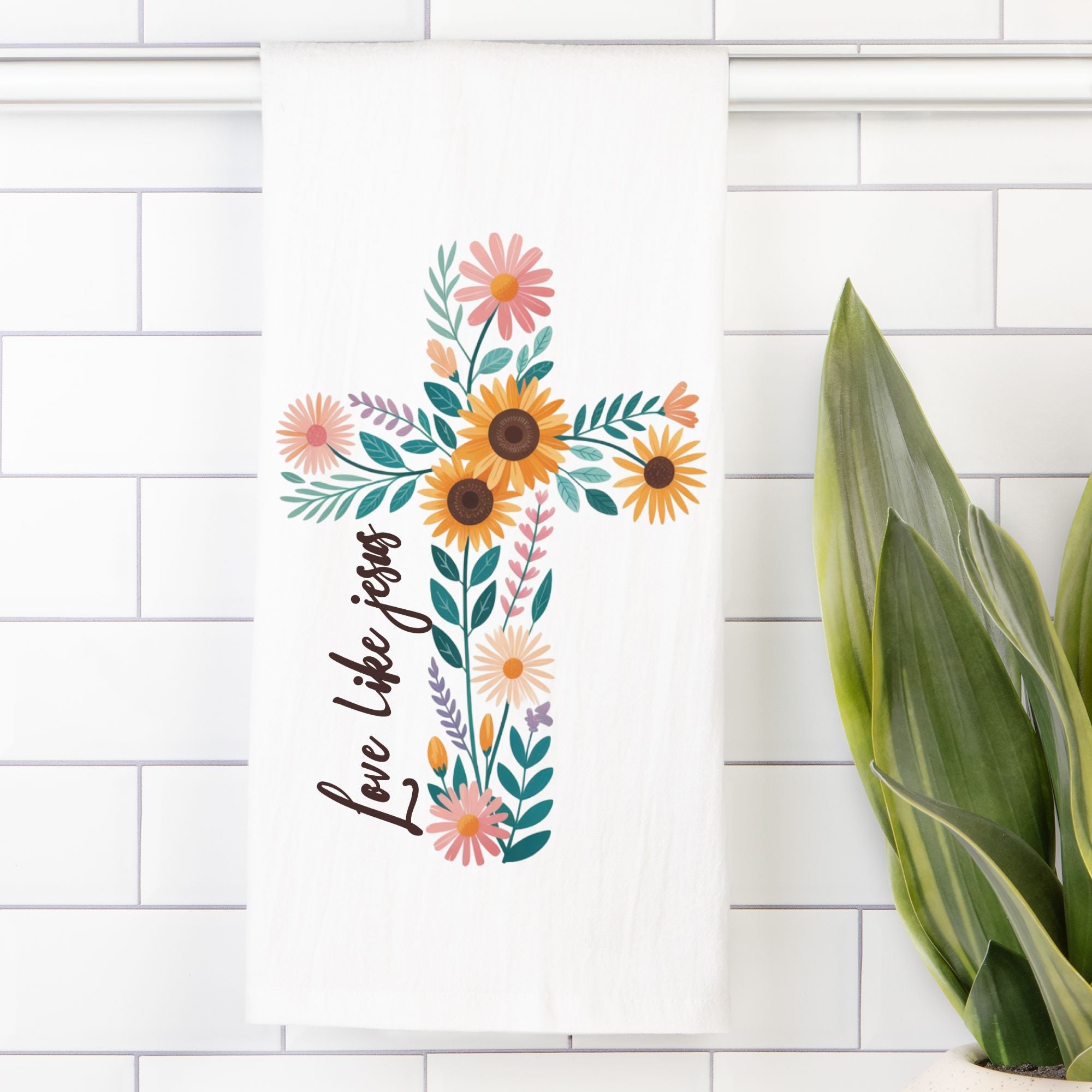 Tea towel with decorative cross with flowers and 'Love Like Jesus' text on a white tiled wall.