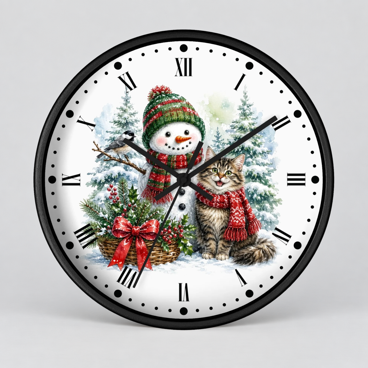 A round wall clock with a black frame and a white face featuring a winter holiday illustration of a snowman and a cat in red scarves, surrounded by pine trees and a basket of greenery. The clock uses black Roman numerals and black hands and dot markers.