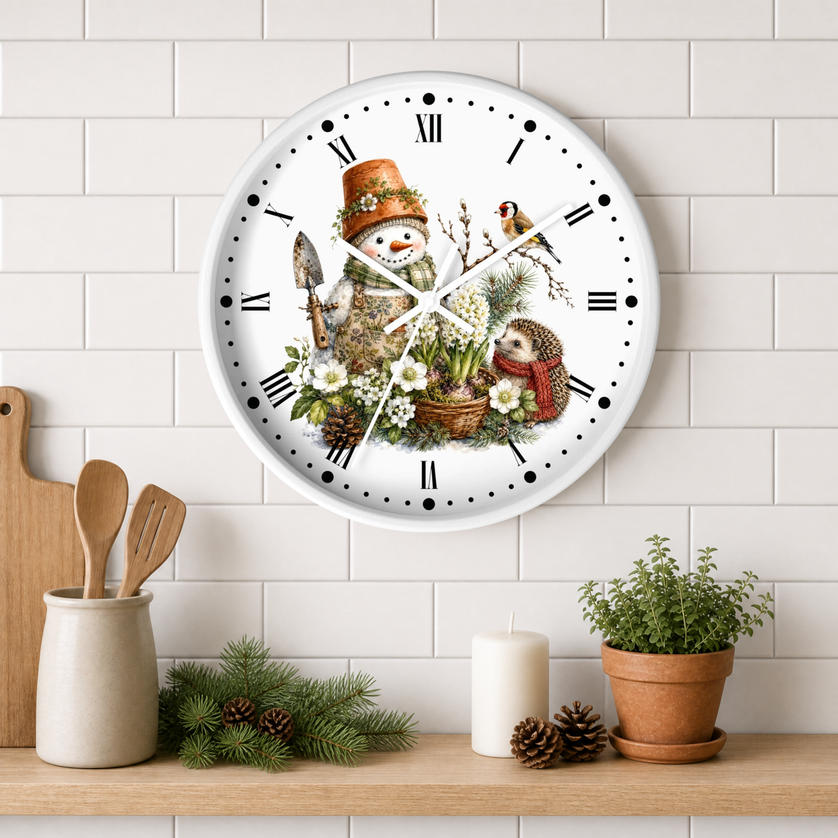 A round white wall clock with a whimsical winter garden illustration, featuring a snowman in a terracotta pot hat, a bird, a hedgehog and flowers, mounted on a white subway tile wall above a wooden shelf with decorative items.
