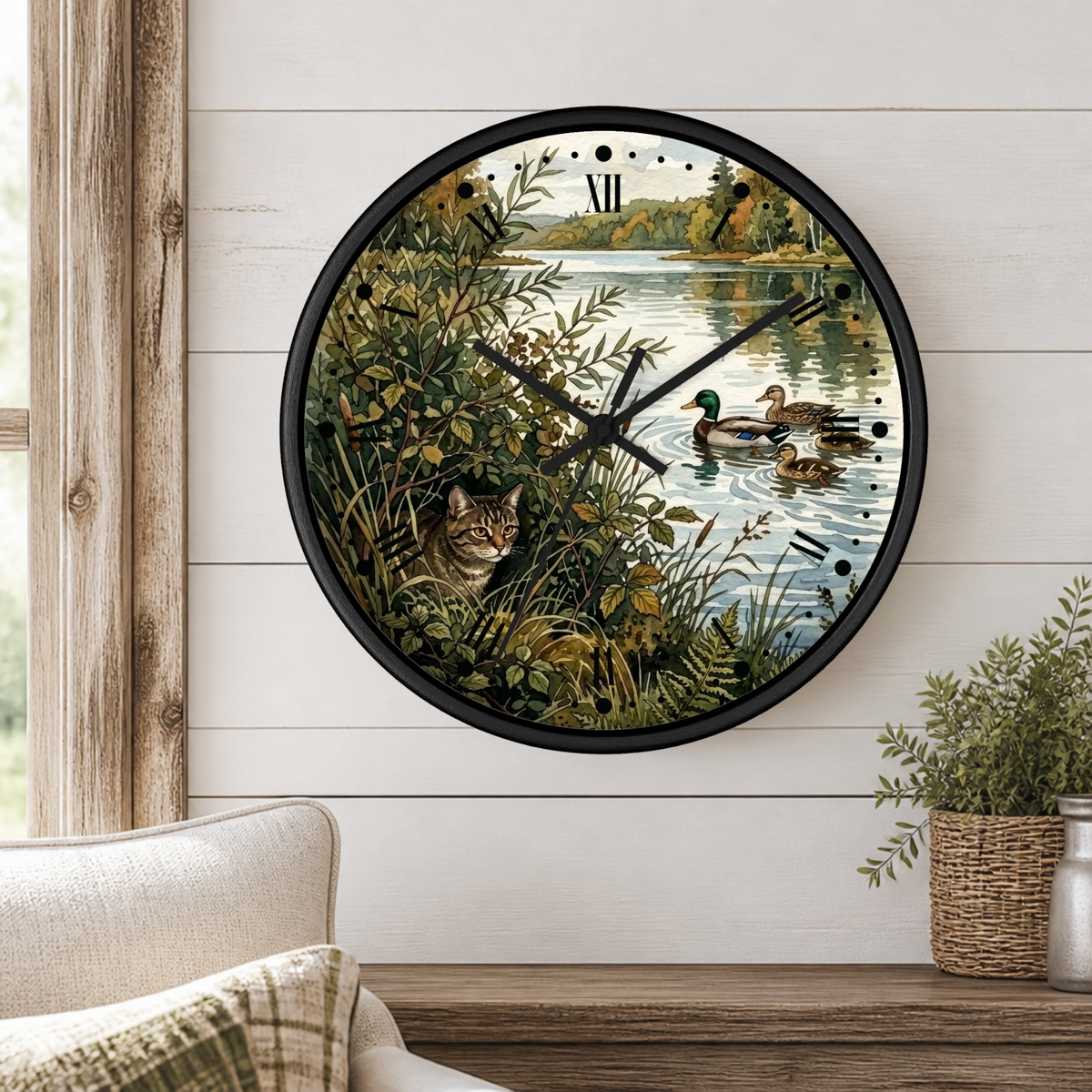 Round wall clock with a black frame and a nature scene print featuring ducks on water and a cat in bushes, mounted on a white shiplap wall above a wooden table with a plant.