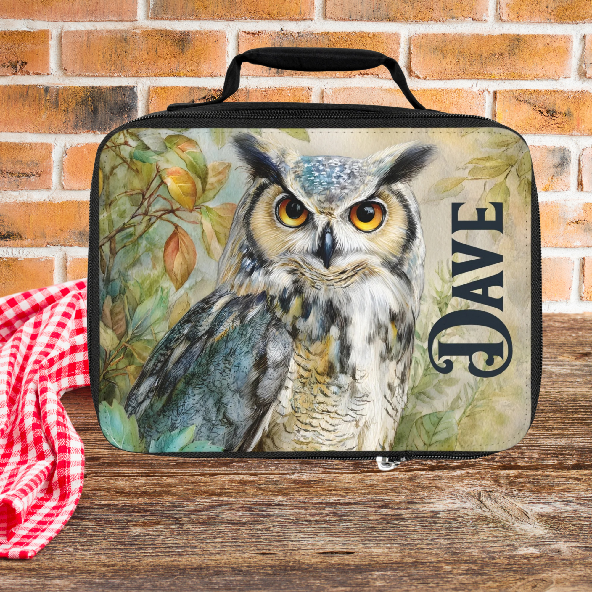Lunch bag with an owl design and 'Dave' text on a wooden picnic table with a brick wall background.
