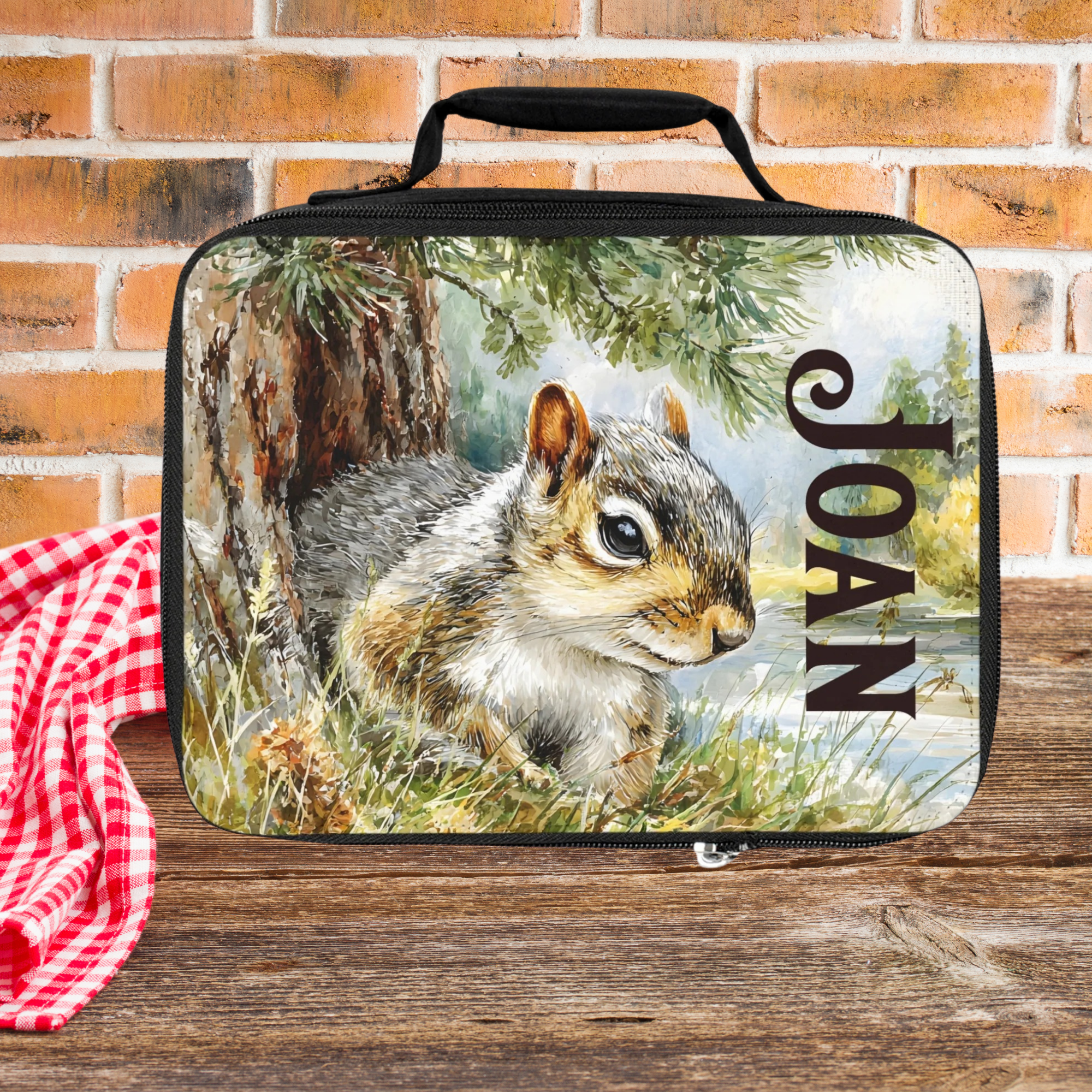 Lunch bag with a squirrel design and the name 'Joan' on a brick wall background