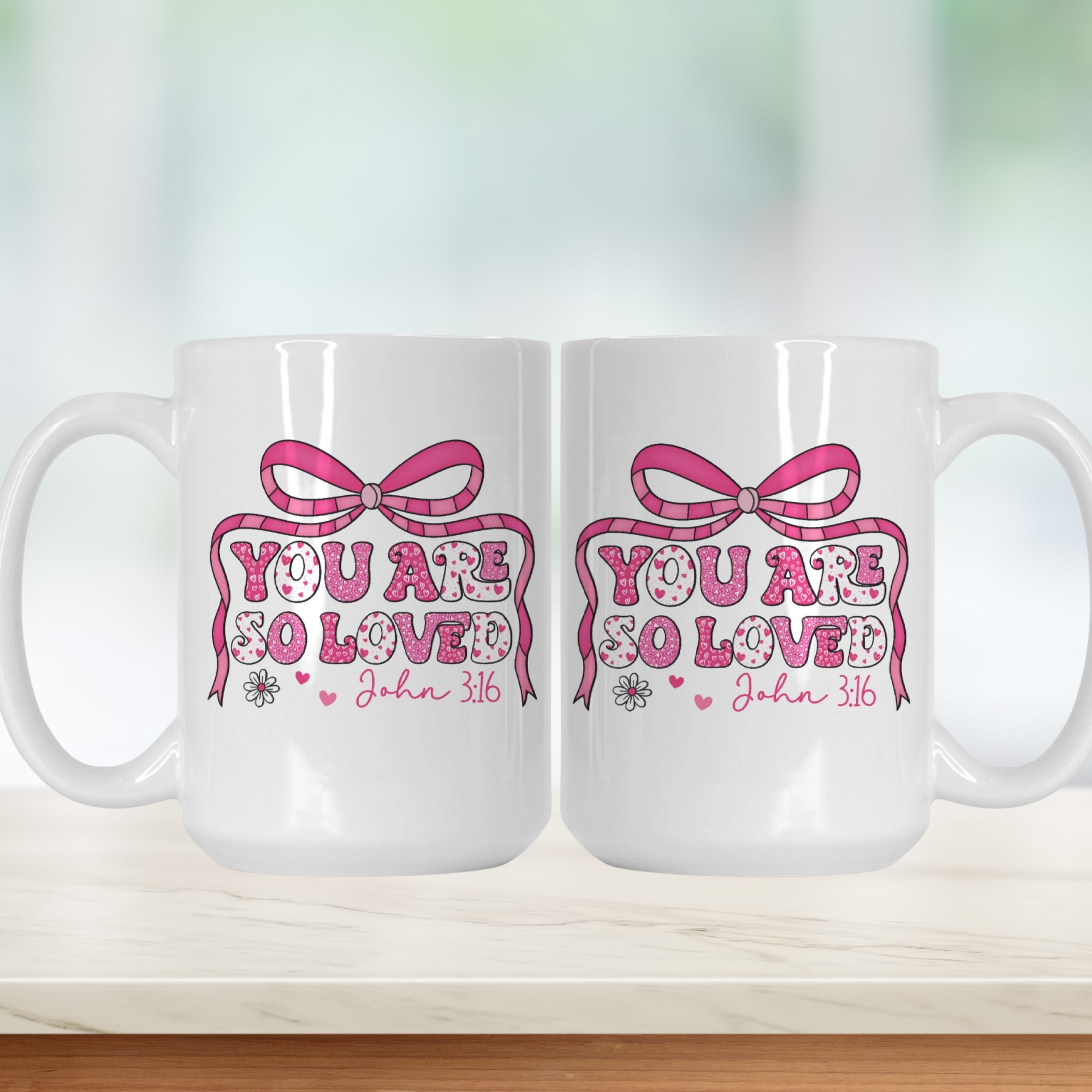 Two white mugs with pink decorative text and graphics on a light background