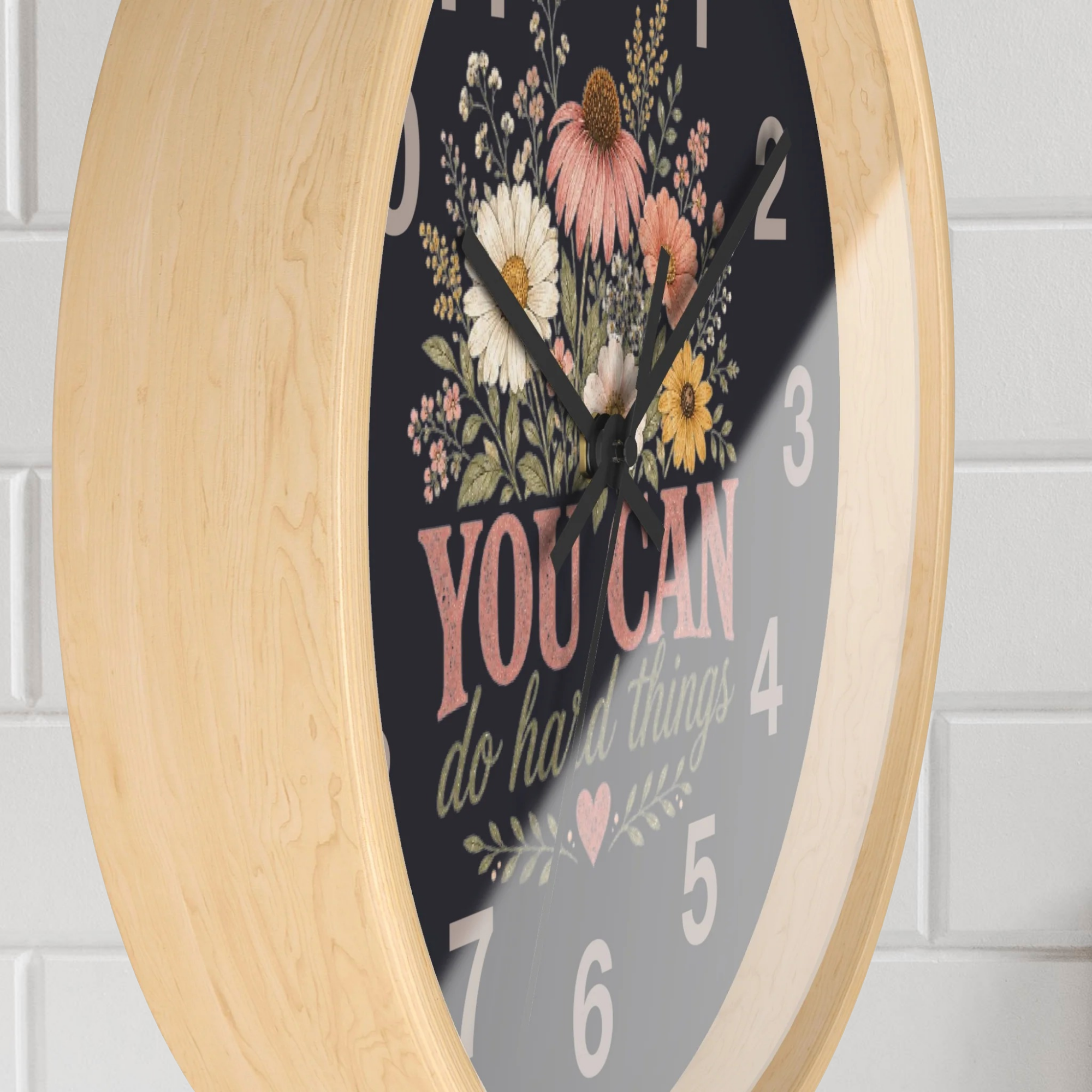 Decorative wall clock with floral design and motivational quote on a light wooden frame.