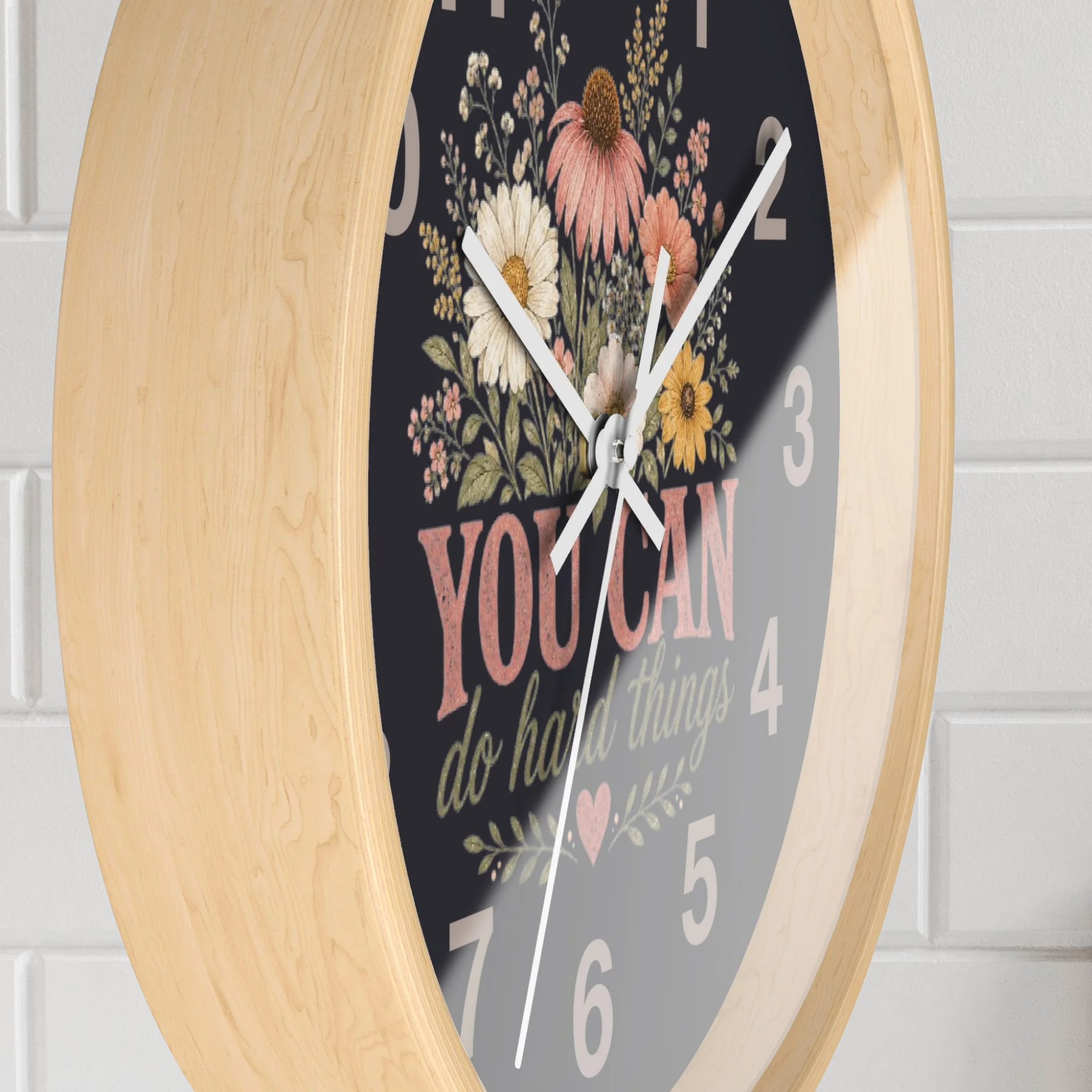 Decorative wall clock with floral design and motivational quote on a light wooden frame.