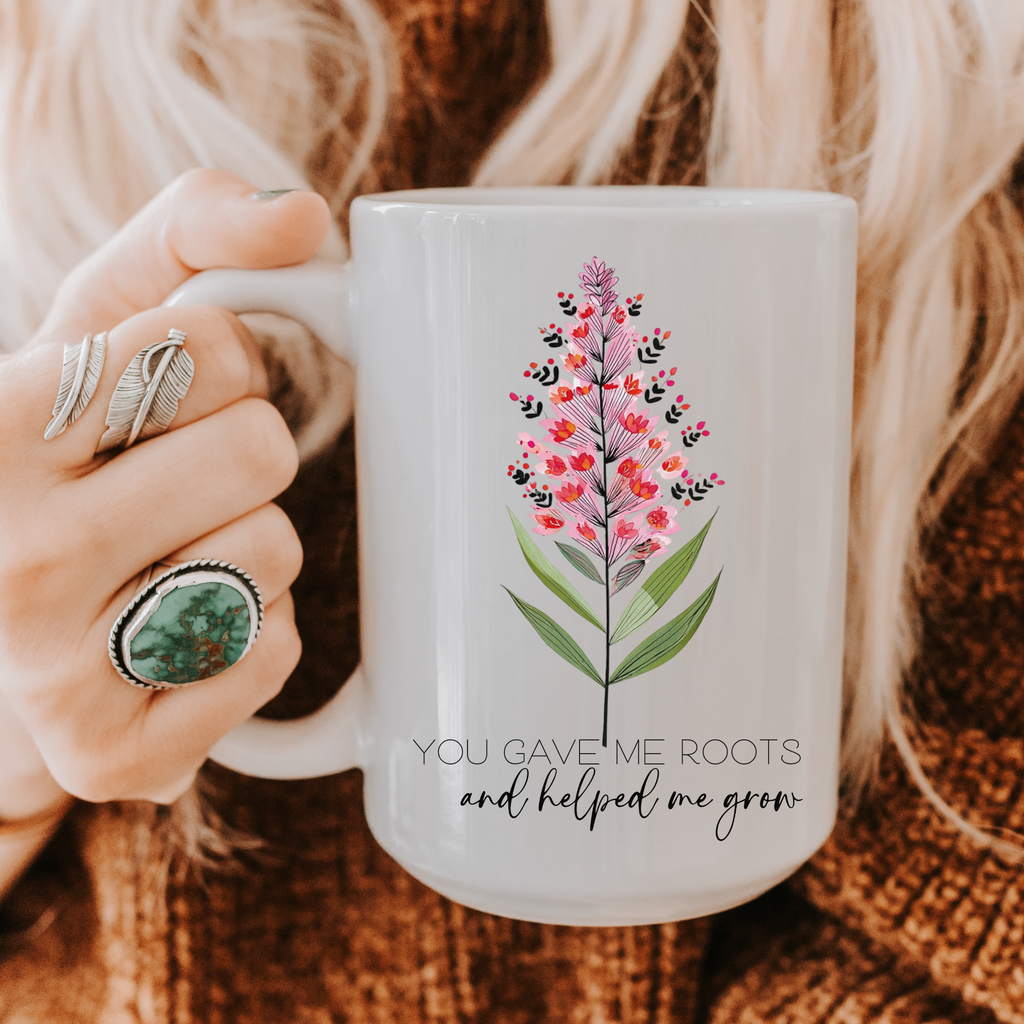 Person holding a 15oz mug with floral design and text 'You Gave Me Roots and Helped Me Grow'.
