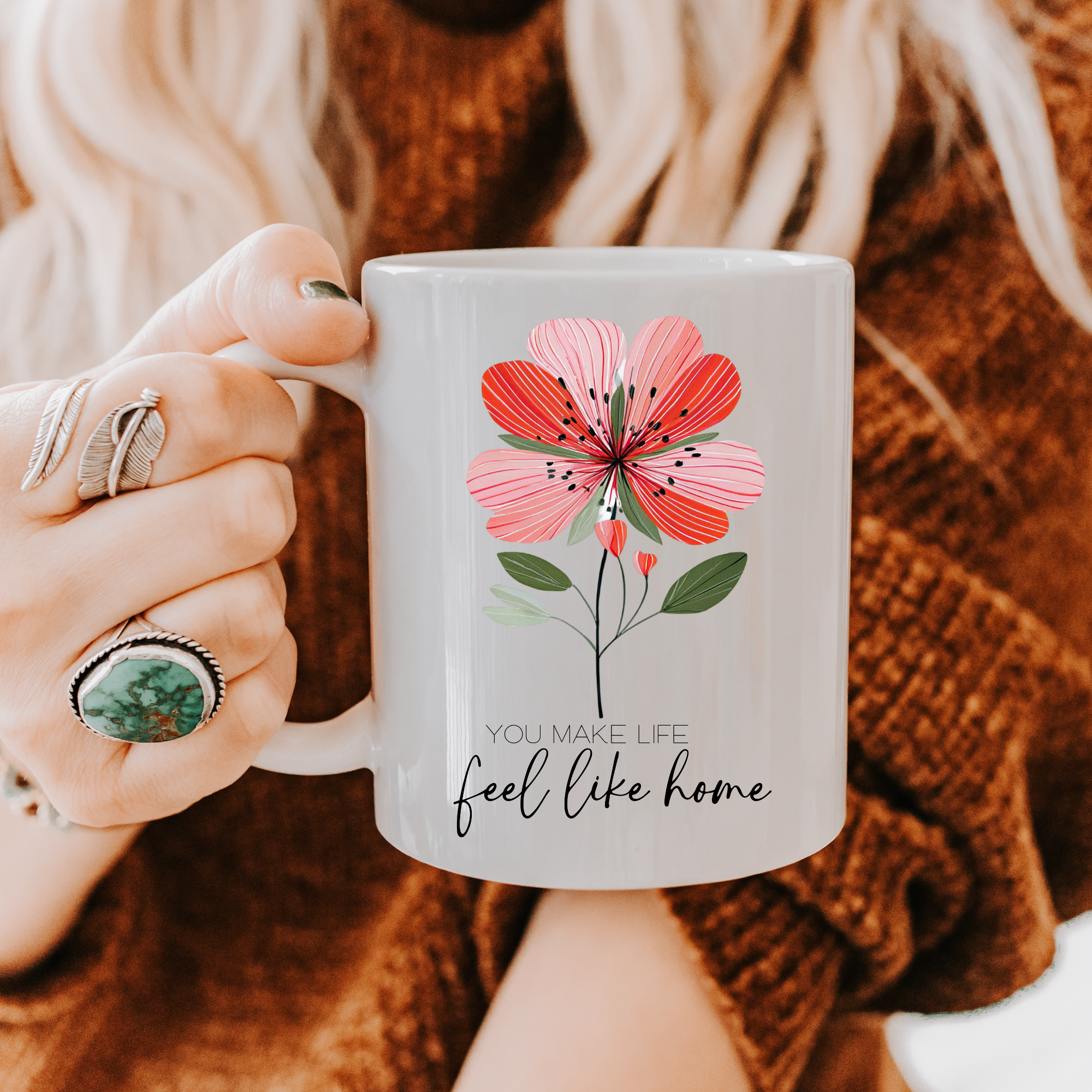 Person holding a 11oz mug with a floral design and text, wearing a brown sweater.