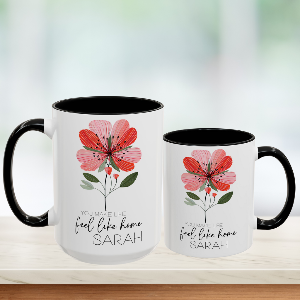 Two white mugs with black handles featuring a red floral design and personalized text on a blurred background.