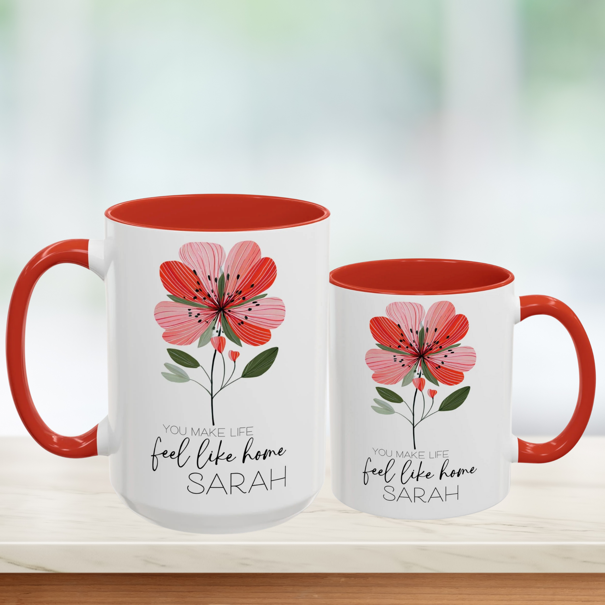 Two white mugs with red interior and handle, featuring floral design and personalized text 'You Make Life Feel Like Home'.