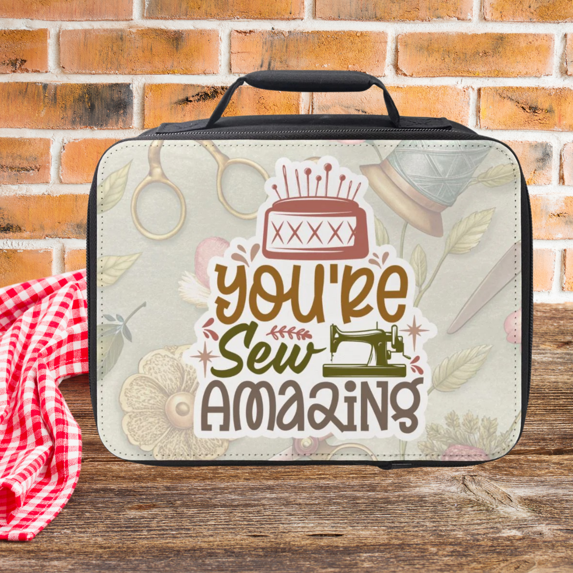 Lunch bag with sewing-themed design and 'You're Sew Amazing' text on a wooden picnic table against a brick wall background.