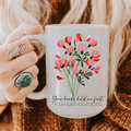 Person holding a 15oz mug with floral design and text 'Your hands held me first your heart holds me still'