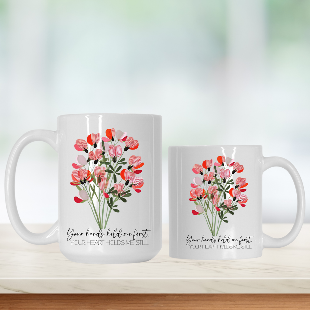 15oz & 11oz white mugs with floral designs and text 'Your hands held me first your heart holds me still' on a light background
