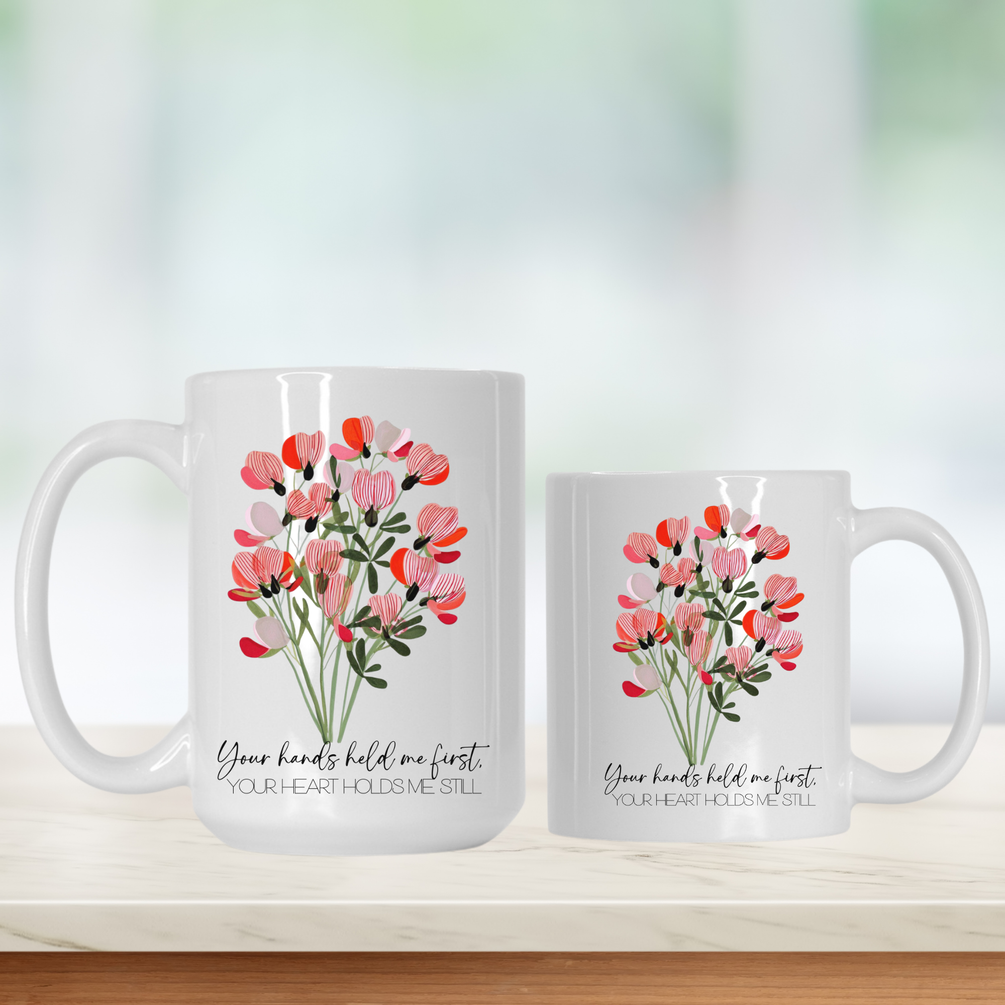 15oz & 11oz white mugs with floral designs and text 'Your hands held me first your heart holds me still' on a light background