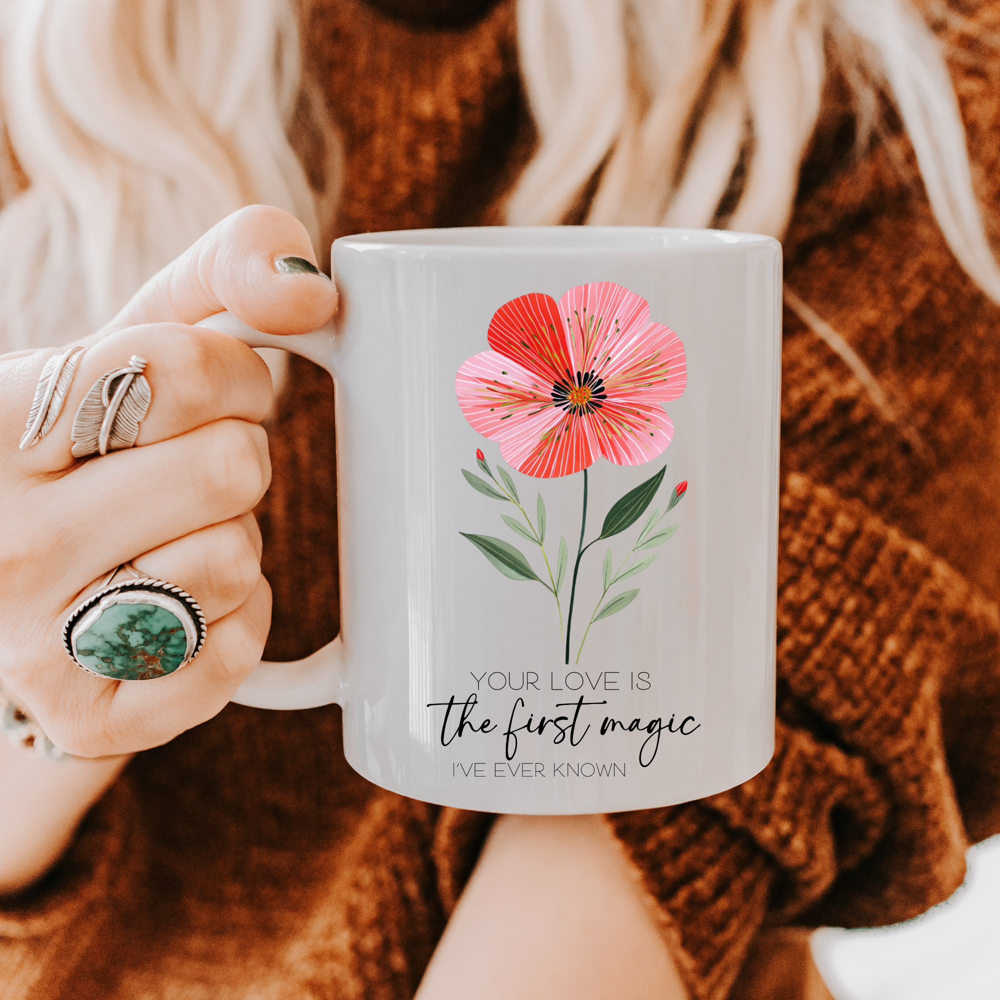 Person holding a 11oz mug with a floral design and text, wearing a brown sweater.
