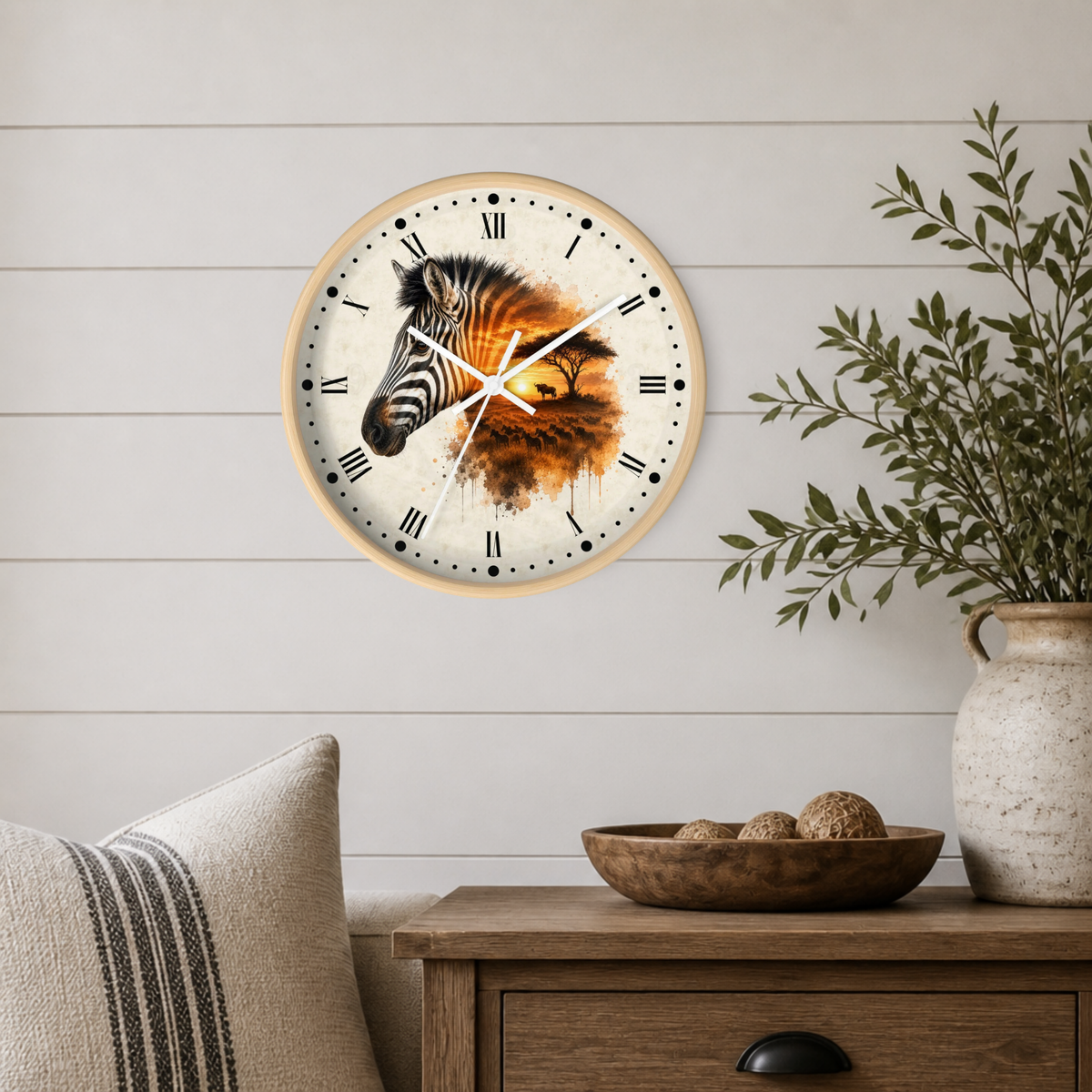 A round wall clock with a zebra and wildebeest illustration, mounted on a white shiplap wall above a wooden side table with a vase and bowl.
