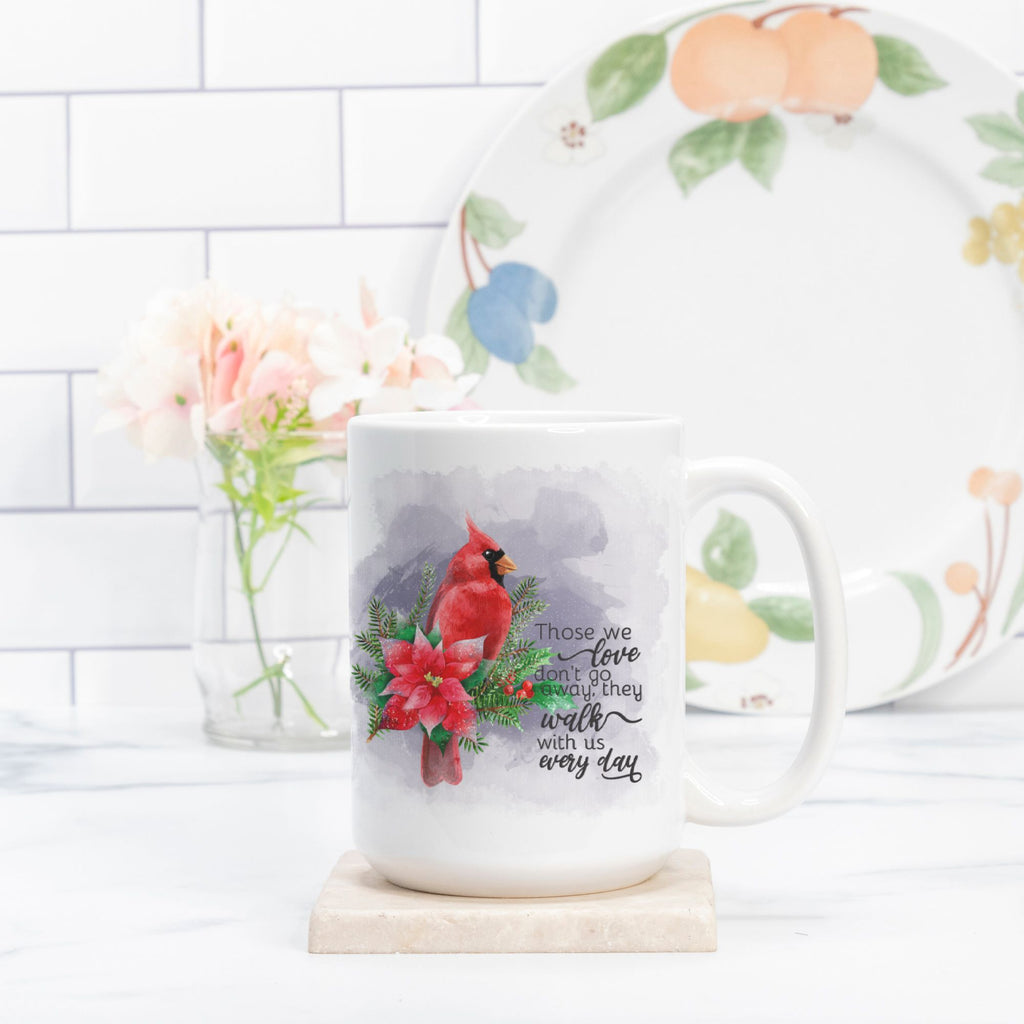 Mug with a cardinal design and text on a white surface with a floral arrangement in the background.