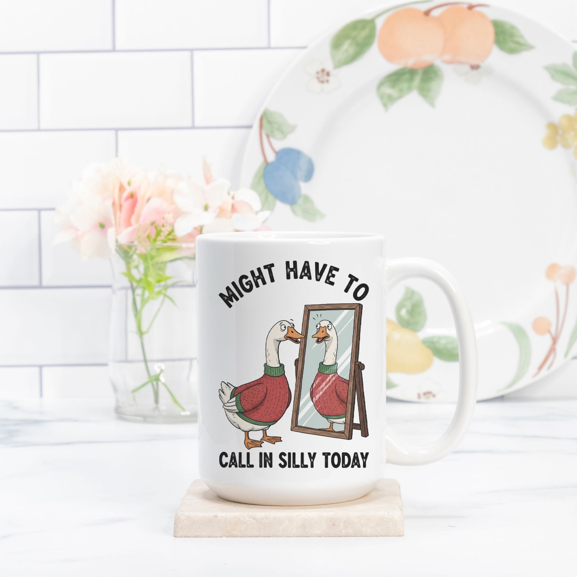 Mug with goose illustration and text on a kitchen counter with a plate and flowers in the background