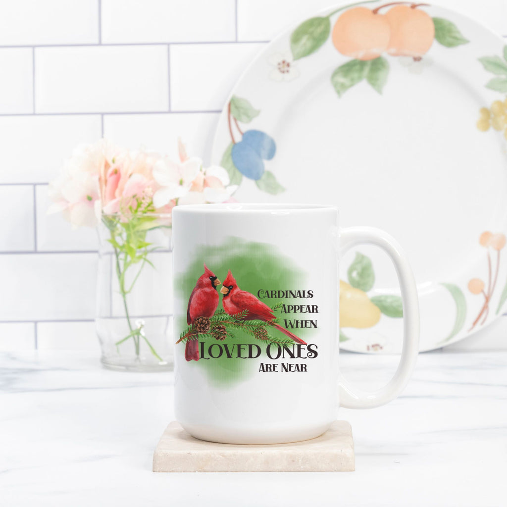 White mug with red cardinals and text on a white surface with a floral plate in the background.