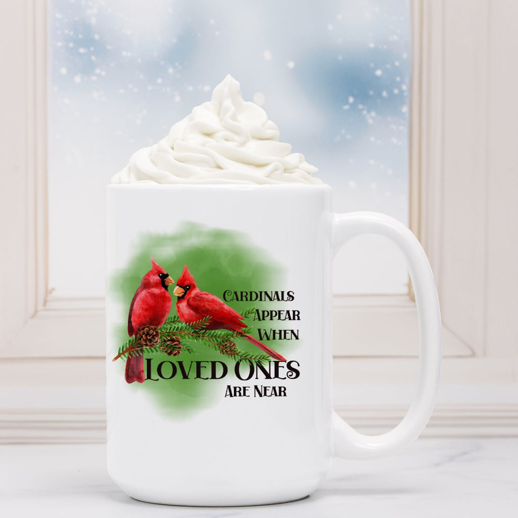 White mug with cardinal design and text, filled with hot chocolate and whipped cream.