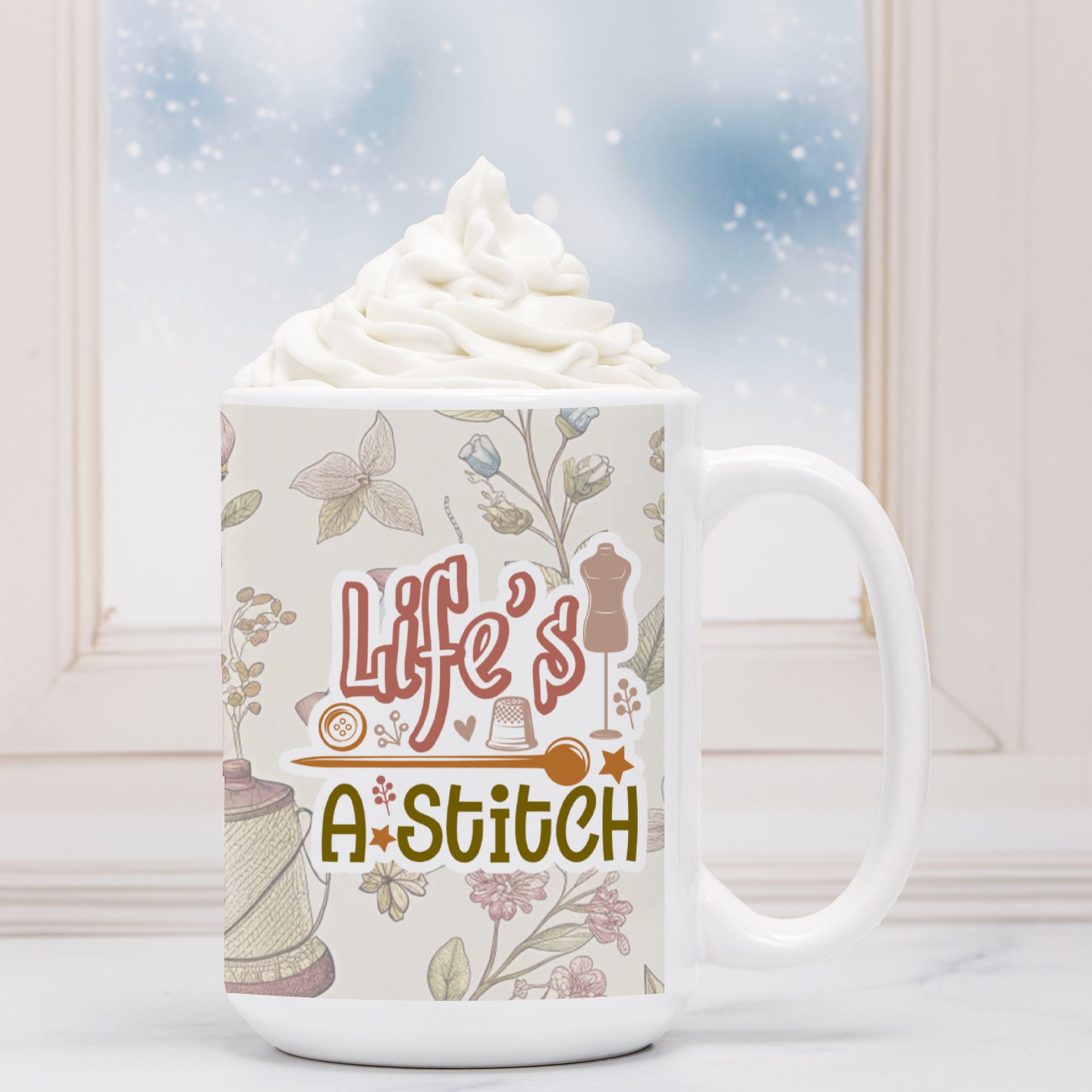 White mug with 'Life's A Stitch' design, filled with hot chocolate and whipped cream, against a light background.