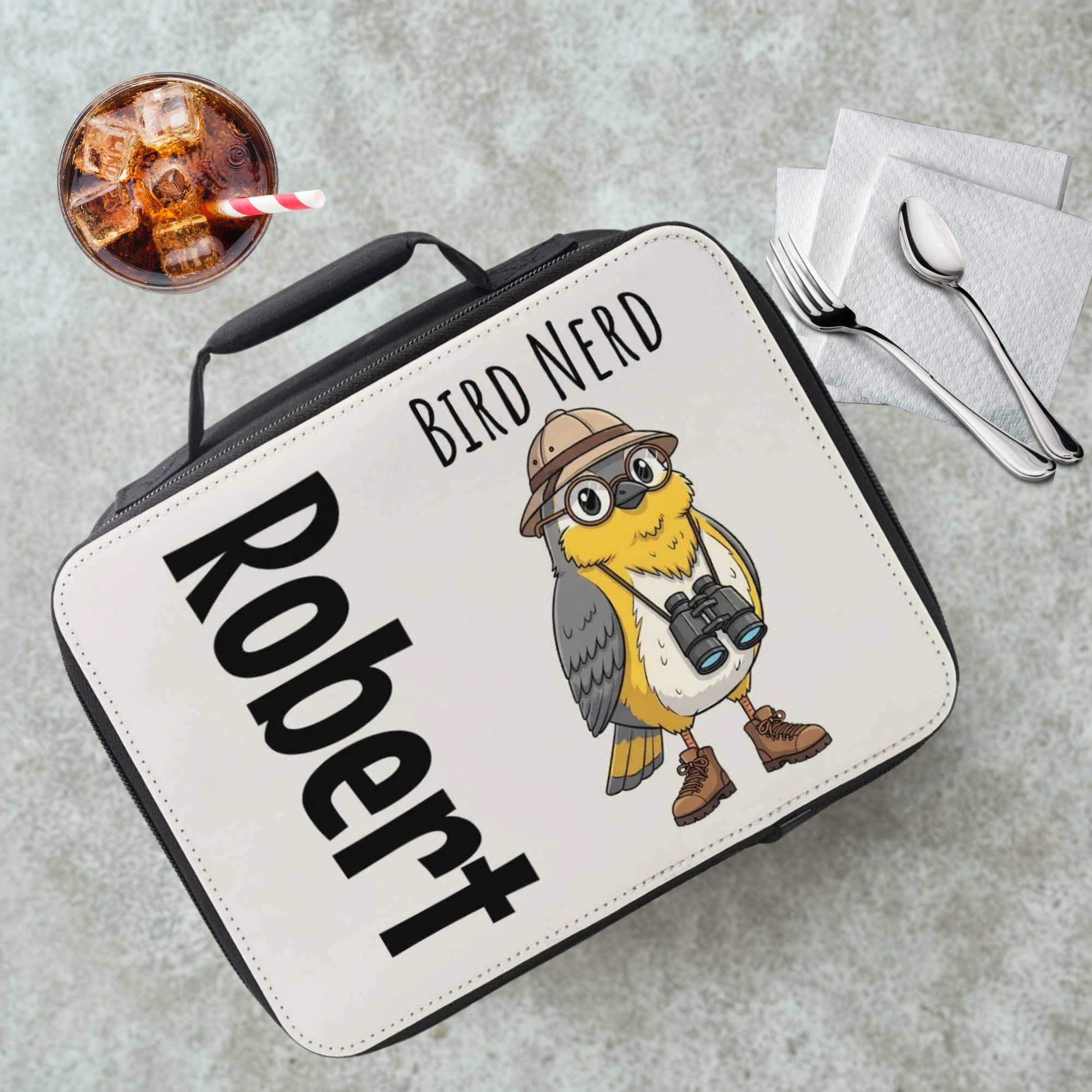 Lunch bag with 'Bird Nerd Robert' design on a gray cafeteria table with a drink and utensils.